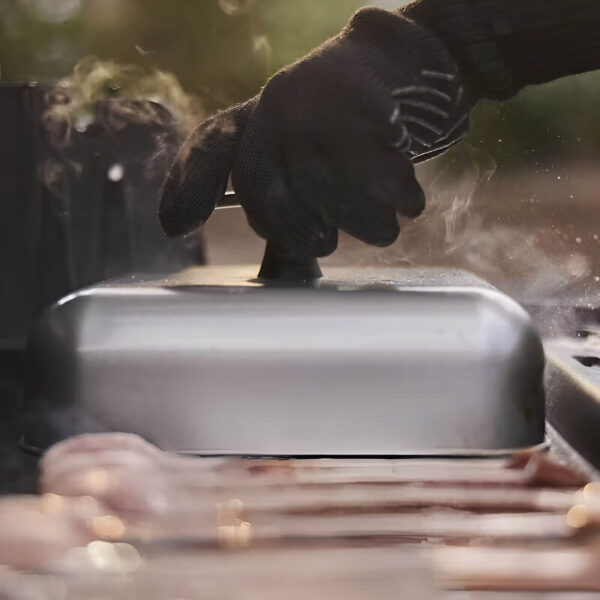 Mano con guante sosteniendo la cubierta para hilvanar hamburguesas Weber sobre una parrilla con vapor.