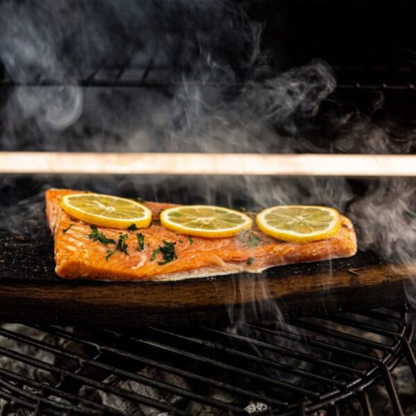 Filete de salmón cocinándose sobre una tabla de barril de whisky en la parrilla, decorado con rodajas de limón y hierbas frescas.