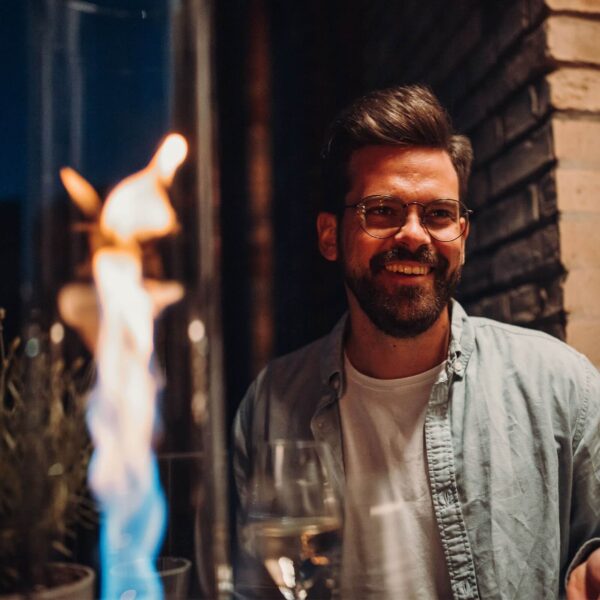 Hombre sonriente disfrutando de una velada junto al fuego de mesa Spin 120 en un ambiente nocturno.