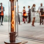 Una lámpara de fuego de mesa Spin 120 de diseño elegante en una terraza de madera con personas socializando al fondo.
