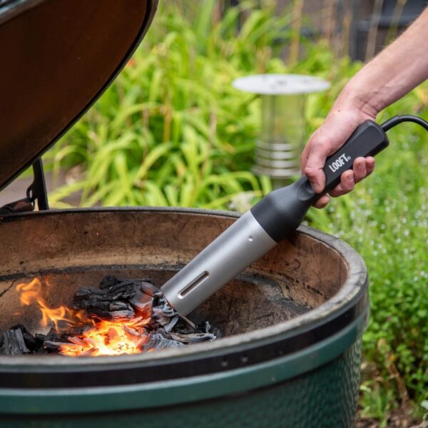 Persona encendiendo carbón en una parrilla de cerámica con el Looft Air Lighter Compact, con fondo de jardín verde.