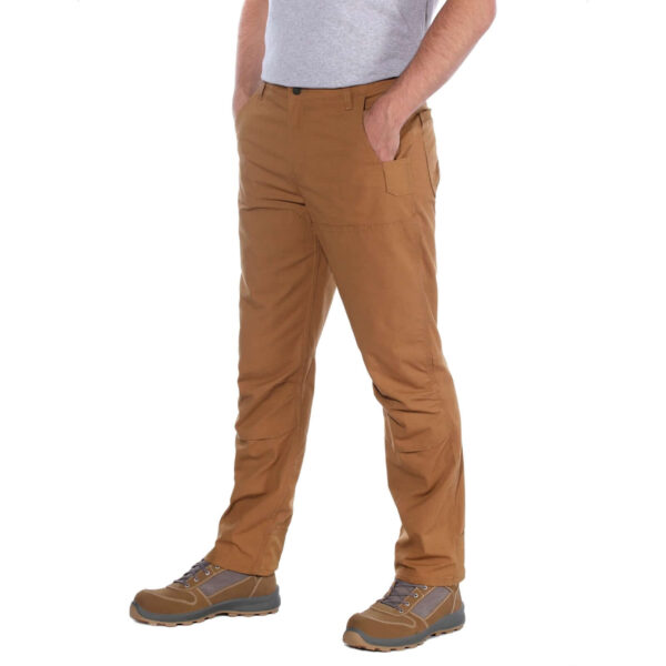 Hombre de pie usando pantalones técnicos Carhartt marrones con manos en los bolsillos.