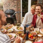 Grupo de personas disfrutando de una comida al aire libre junto a una barbacoa Weber Q 2800N+ en un patio acogedor.