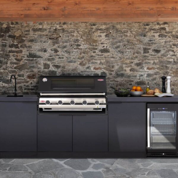 Cocina de exterior Cabinex® en un ambiente cubierto con pared de piedra, equipada con barbacoa, fregadero negro mate y nevera exterior.