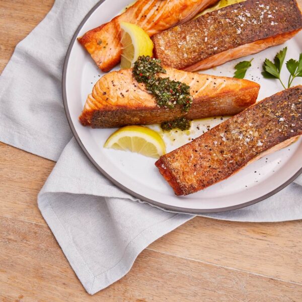 Plato de filetes de salmón a la parrilla servidos con aderezo de hierbas frescas y rodajas de limón sobre un fondo de madera.