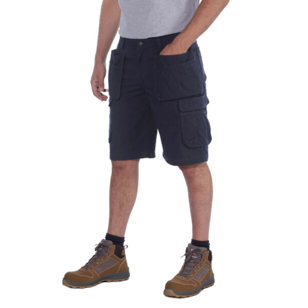 Hombre usando un pantalón corto multibolsillos Carhartt en azul marino, con las manos en los bolsillos, visto en ángulo.