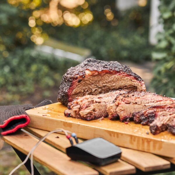 Brisket perfectamente cocido sobre una tabla de madera con el Weber Connect Smart Grilling Hub en primer plano.