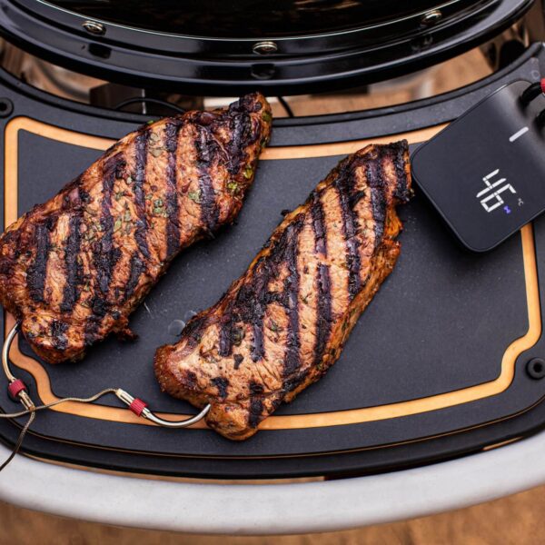 Dos cortes de carne asada con marcas de parrilla en una plancha, monitoreados por el Weber Connect Smart Grilling Hub.