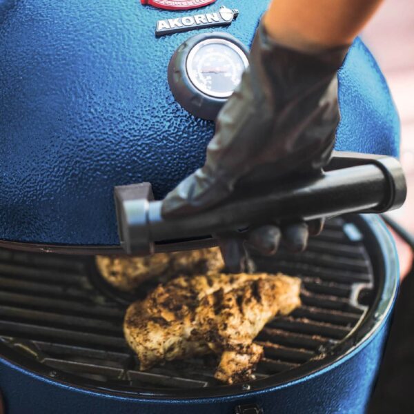 Persona abriendo una parrilla kamado Akorn con pollo a la parrilla en cocción.