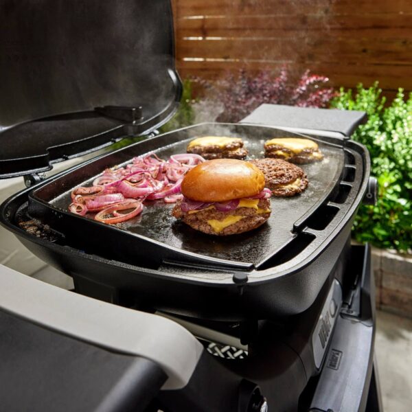 Hamburguesas con queso y cebolla caramelizada cocinándose en la plancha de hierro fundido de una parrilla Weber Q2000N.