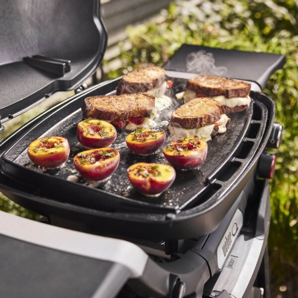 Sándwiches de queso derretido y duraznos asados cocinándose en la plancha de hierro fundido de una parrilla Weber Q2000N.