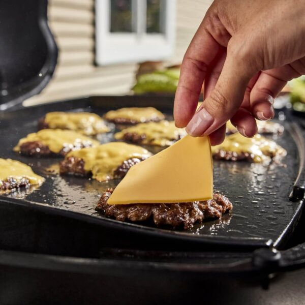 Mano colocando una rebanada de queso sobre una hamburguesa en la plancha de hierro fundido de una parrilla Weber Q2000N.