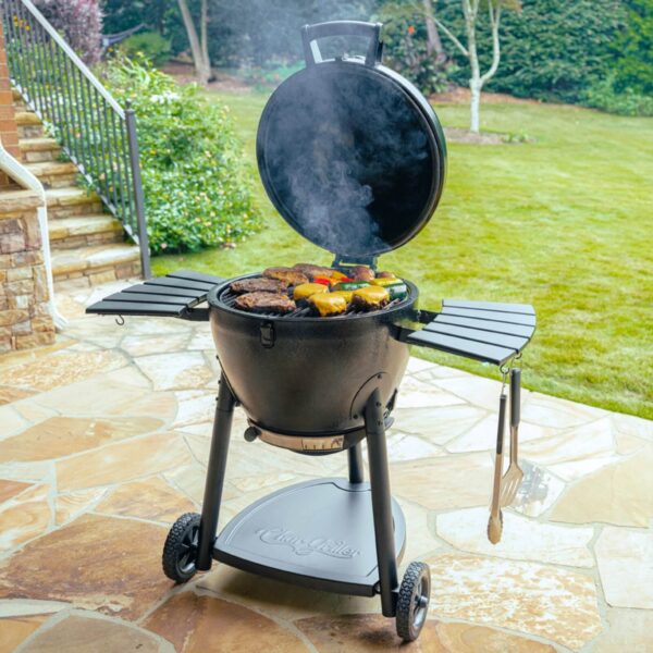 Kamado Akorn Normal de CharGriller cocinando carne y vegetales, en un patio exterior con tapa abierta y humo saliendo.