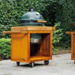 Mesa Kamado OFYR pequeña con barbacoa Big Green Egg en jardín con vegetación.
