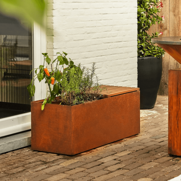 Jardinera con plantas aromáticas y un banco de acero corten en un patio exterior.