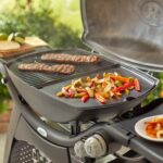 Barbacoa Weber Q 3000 con plancha de hierro colado vitrificado, cocinando fajitas de pimientos y carne a la parrilla.