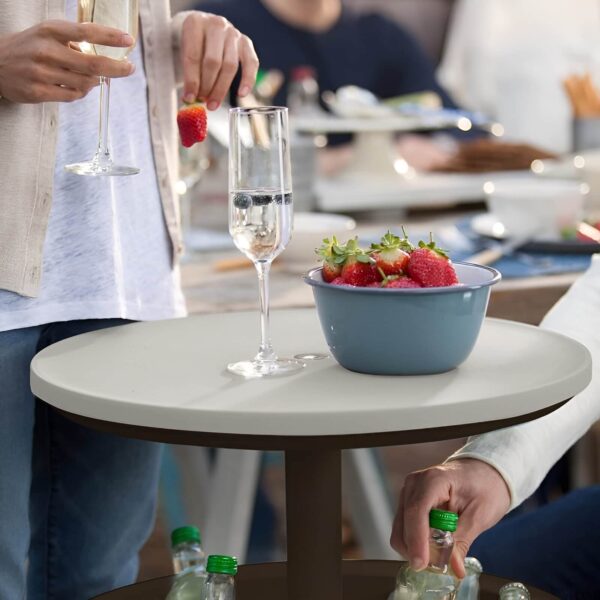 Primer plano de la Mesa Nevera CoolBar de Keter con una copa de vino espumoso y un bol de fresas en la tapa, mientras una persona toma una botella del compartimento inferior.