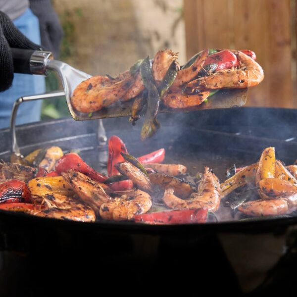 Espátula levantando camarones y vegetales asados en una plancha caliente, ideal para preparar mariscos y guarniciones.