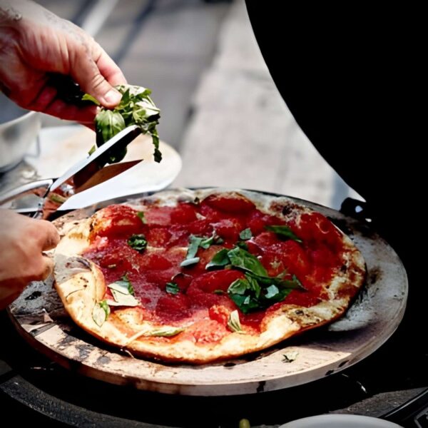 Persona agregando albahaca fresca sobre una pizza cocinada en la piedra de pizza The Bastard en una parrilla.