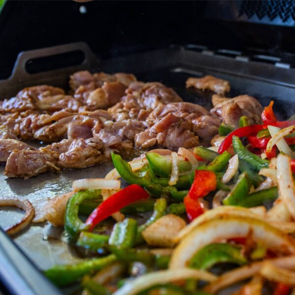 Pollo y vegetales cocinándose en la plancha de acero inoxidable Napoleon sobre una parrilla Freestyle o Rogue 425.