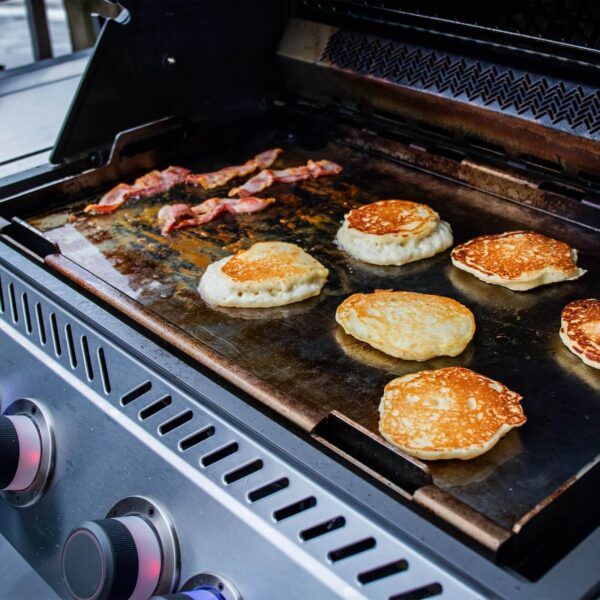 Panqueques dorados y tocino cocinándose en la plancha de acero inoxidable Napoleon sobre una parrilla Prestige PRO, Prestige, Built-in 700, Rogue 525 o 625.