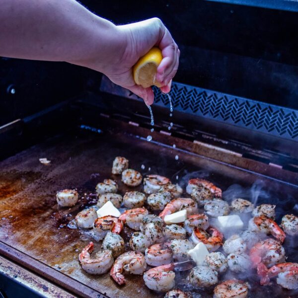 Gambas doradas con mantequilla y jugo de limón cocinándose en la plancha de acero inoxidable Napoleon.