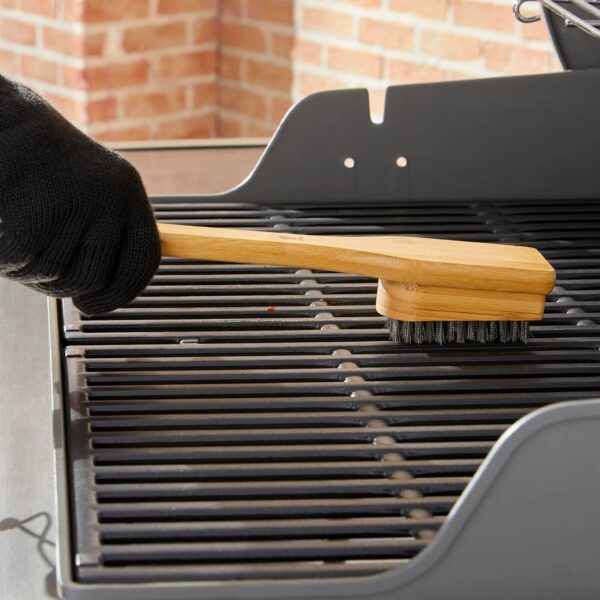 Persona con guantes negros limpiando una parrilla de gas con el cepillo de bambú Weber de 45 cm.