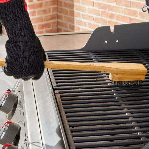 Persona con guantes de protección limpiando una parrilla de gas con el cepillo de bambú Weber de 45 cm.