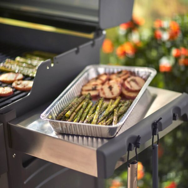 Bandeja de aluminio Weber con espárragos y papas asadas junto a una parrilla encendida.