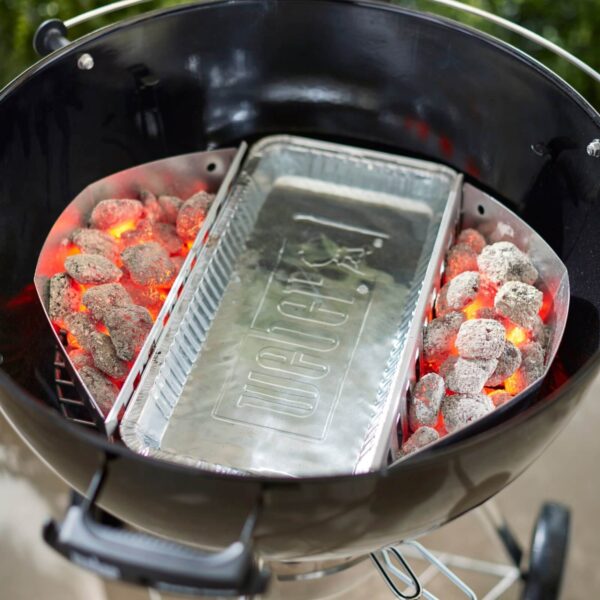 Bandeja de aluminio Weber colocada en el centro de una parrilla con carbón encendido para cocinar con calor indirecto.