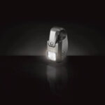 Luz LED encendida con diseño moderno, montada en un soporte curvo, iluminando un fondo oscuro.