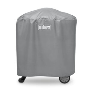Funda Weber® Estándar Q1000/Q2000 de color gris cubriendo una barbacoa de la Serie Q con carro, con logo blanco en la parte superior y ruedas visibles en la base.