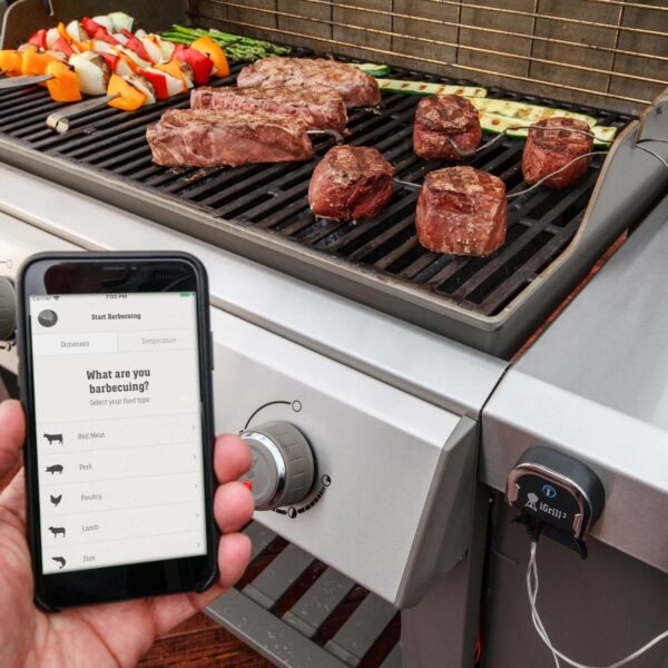 Parrilla de gas con termómetro iGrill 3 de Weber integrado, monitoreando la temperatura de la carne a través de un smartphone.