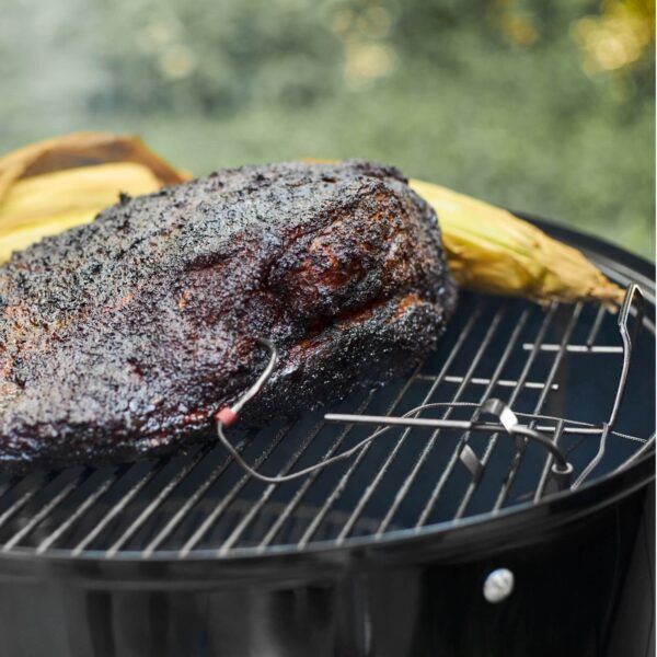 Sonda de temperatura Weber monitoreando un corte de carne en una parrilla junto a un elote asado.