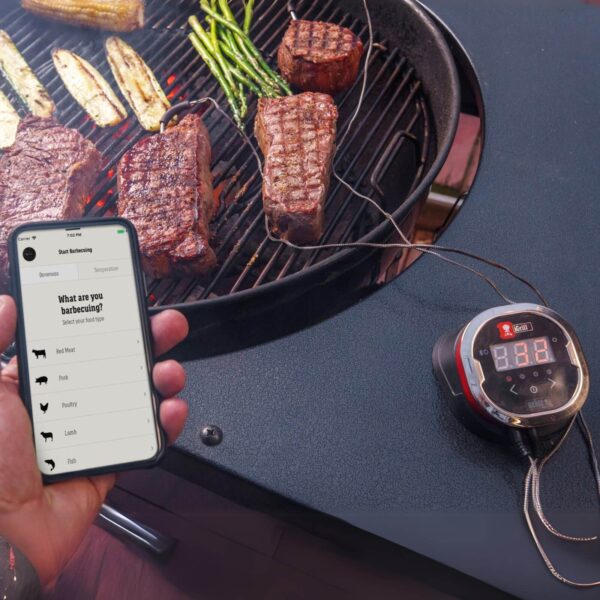 Termómetro iGrill 2 de Weber monitoreando la temperatura de cortes de carne en una parrilla, con control desde un smartphone.