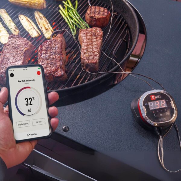 Termómetro iGrill 2 de Weber monitoreando la temperatura de un New York strip steak en una parrilla, con control desde un smartphone.