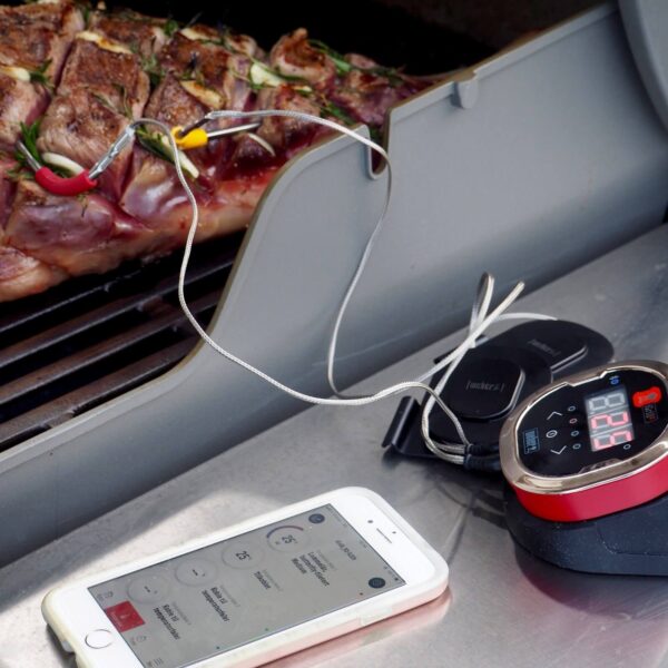 Termómetro iGrill 2 de Weber monitoreando la temperatura de un corte de carne en la parrilla, con control desde un smartphone.