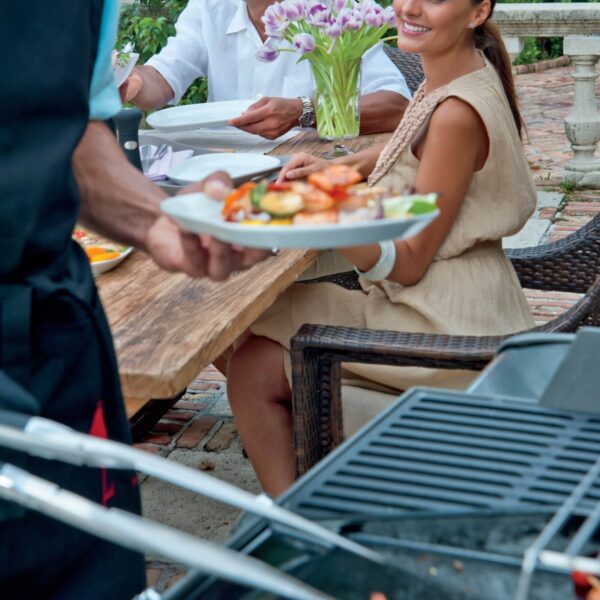 Cena al aire libre con platos preparados en la barbacoa Weber Spirit con la Plancha Deluxe, sirviendo mariscos y verduras.