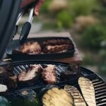 Carne y vegetales asados sobre una plancha de hierro fundido en una parrilla al aire libre.