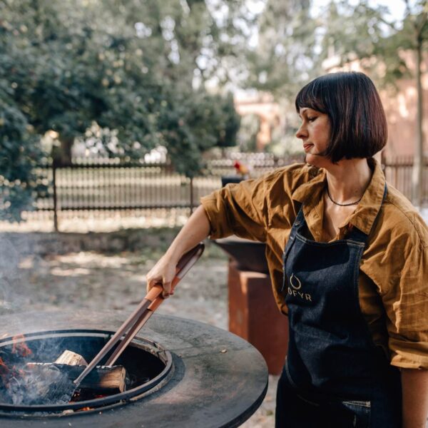 Mujer manipulando leña en una barbacoa al aire libre usando las pinzas del Juego Buffadoo.