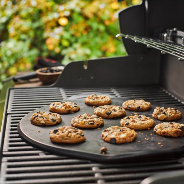 Galletas caseras horneadas sobre la piedra de barbacoa Weber en una parrilla al aire libre, con un fondo de vegetación.