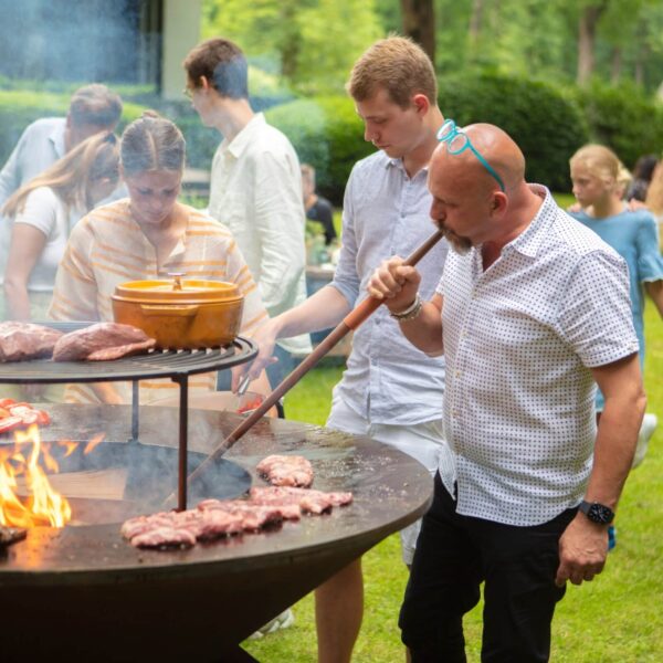 Grupo de personas disfrutando de una barbacoa al aire libre, mientras un hombre usa el Juego Buffadoo para avivar el fuego.