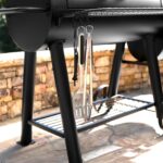 Ganchos para utensilios en la barbacoa Competition Pro de Char-Griller con espátula, pinzas y accesorios colgados.