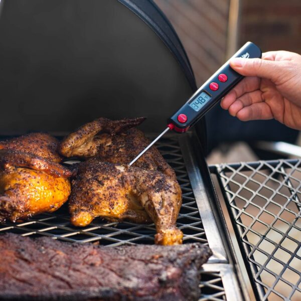 Mano utilizando un termómetro digital para medir la temperatura interna de un pollo asado en la barbacoa Competition Pro de Char-Griller.