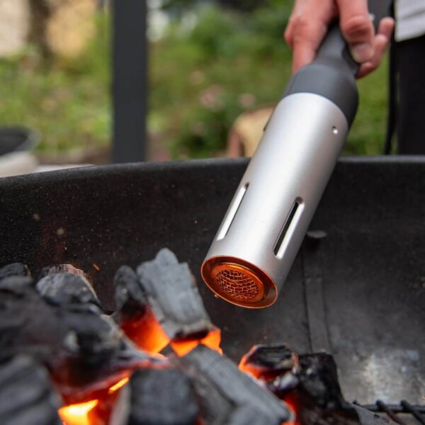 Primer plano del Looft Air Lighter Compact encendiendo carbón, con detalle del flujo de aire caliente y las brasas en una parrilla.