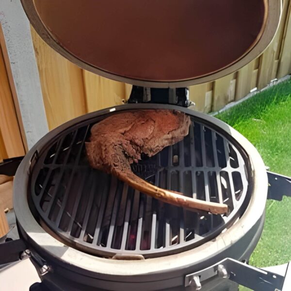 Un corte de carne tomahawk cocinándose sobre la parrilla de hierro fundido The Bastard en una parrilla cerámica.