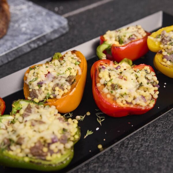 Primer plano de pimientos rojos, amarillos y verdes rellenos de couscous, queso y hierbas frescas.