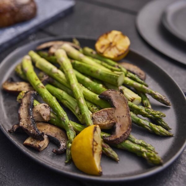 Espárragos verdes y champiñones a la parrilla servidos en un plato, acompañados de un limón asado.