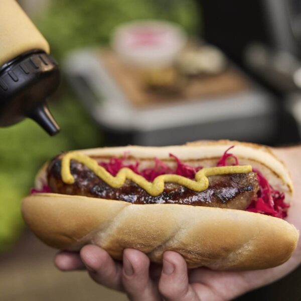 Hot dog con salchicha asada, col morada y mostaza amarilla en un pan suave, listo para disfrutar.