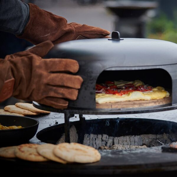 Persona usando guantes de gamuza marrones para manipular un horno para pizzas caliente al aire libre, mostrando su resistencia al calor y utilidad en la cocina.